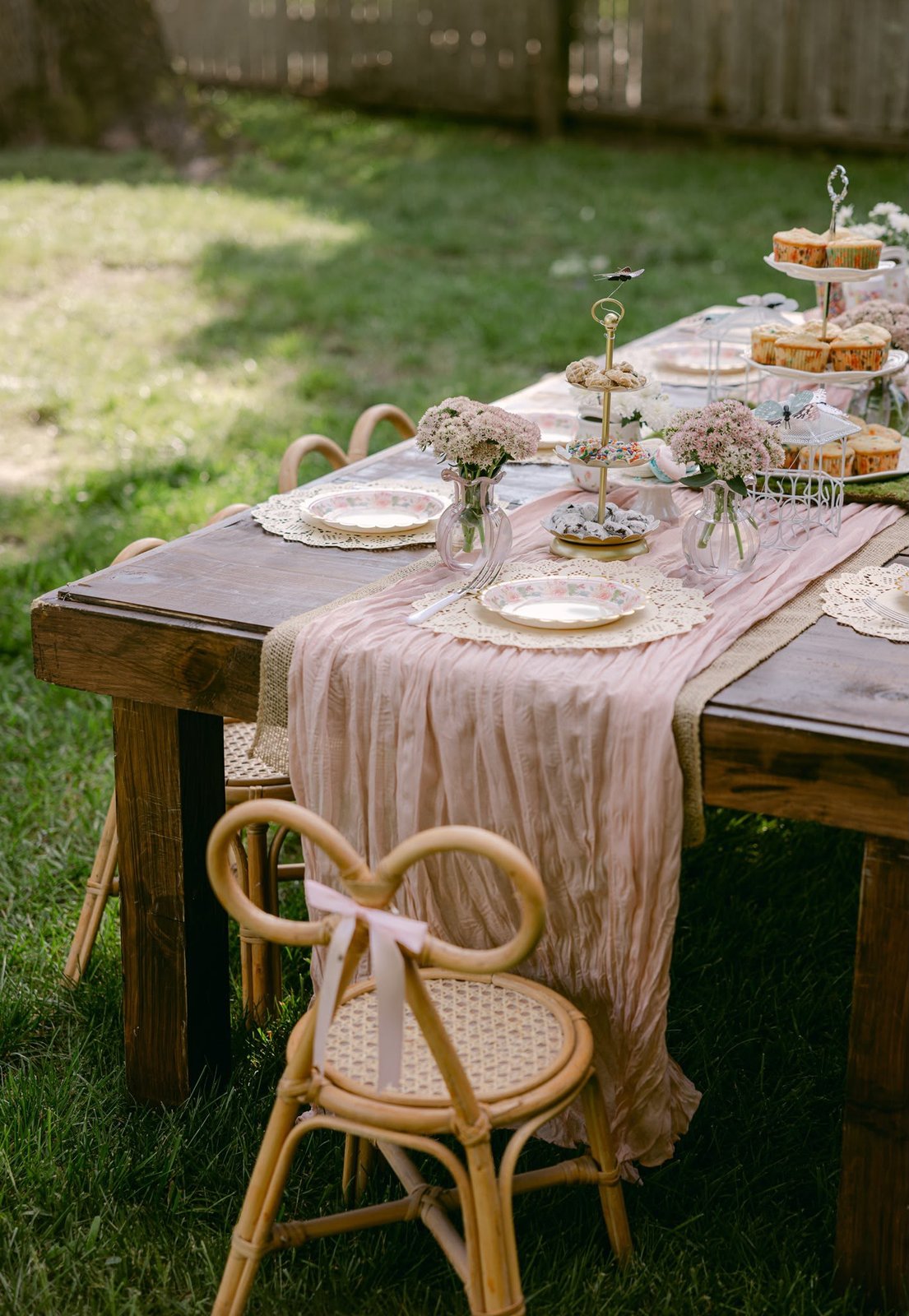 Styled dessert and food station on a wooden table with tiered stands and bow-back kids' chairs