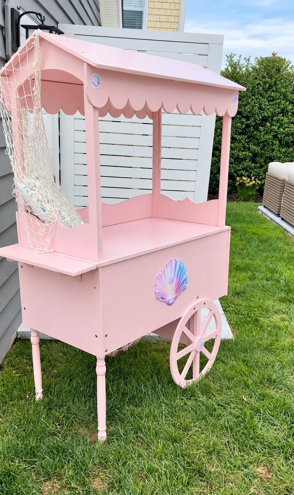 Pink wooden children's dessert cart with a scalloped canopy set up on a lawn ready for treats